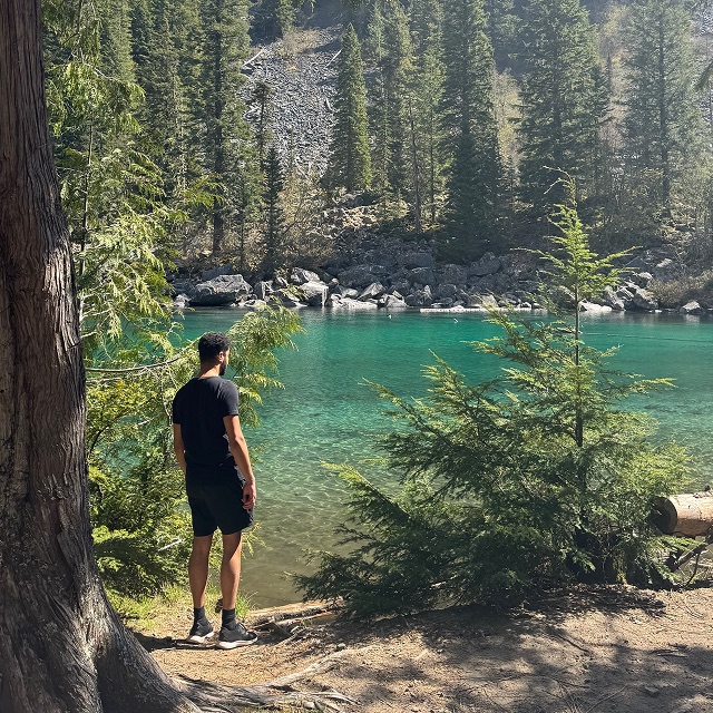 Andy on a forest trail looking out over a turquoise mountain lake
